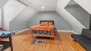 Een slaapkamer met een loft-stijl plafond, een bed met oranje beddengoed, een zwarte bank en een pooltafel.