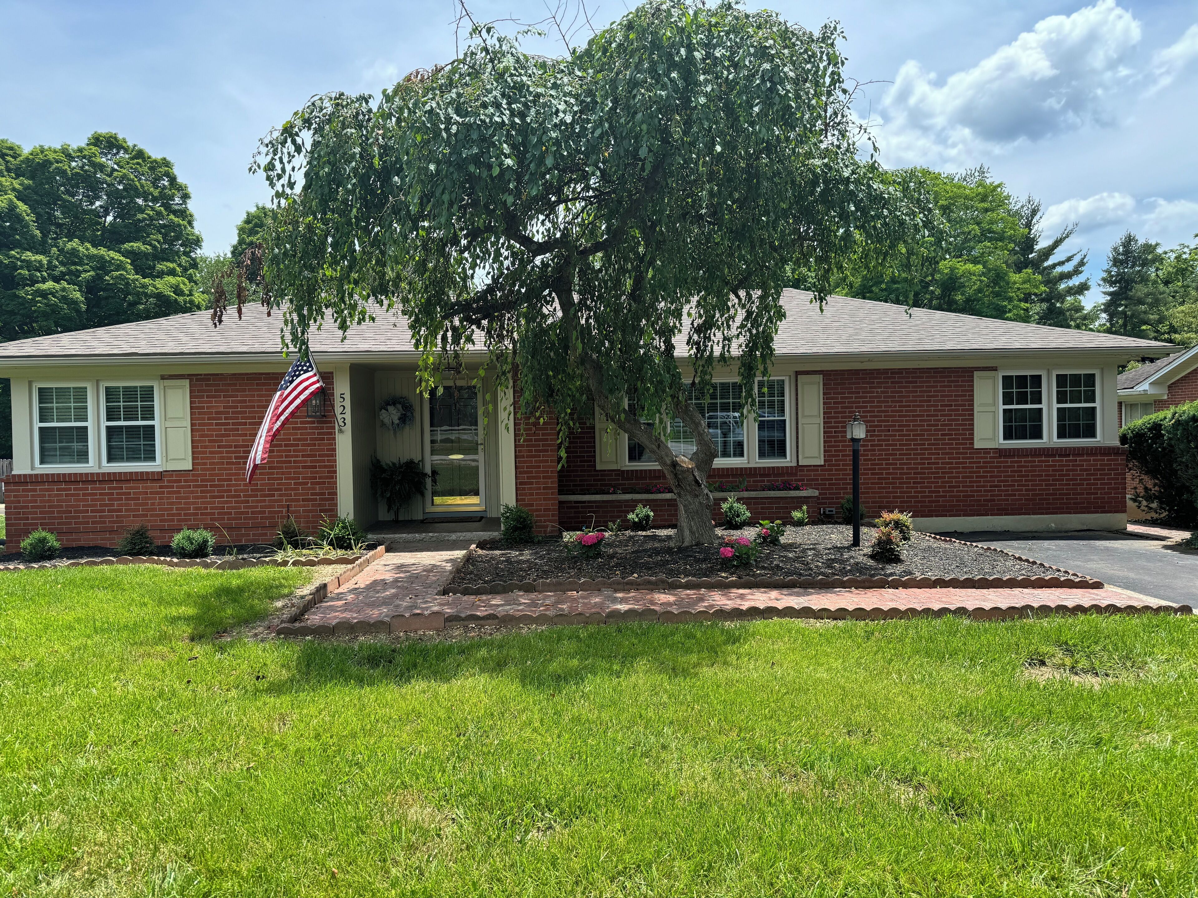A brick house with a front porch, a tree, and a well-maintained lawn.