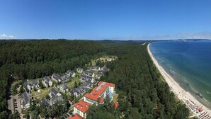An aerial view of a coastal residential area with houses, a beach, and a forested hill.