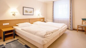 Een hotelkamer met twee bedden, een tafeltje, een stoel en een raam met gordijnen.