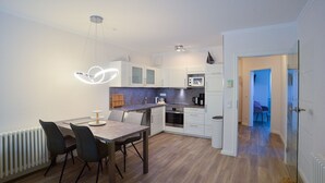 A modern kitchen with white cabinets, a wooden dining table, and a unique pendant light.