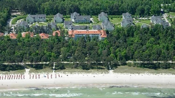 An aerial view of a coastal resort with multiple buildings, a beach, and a forested area.