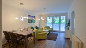 A modern living room with a dining table, green sofas, and a ceiling light fixture.