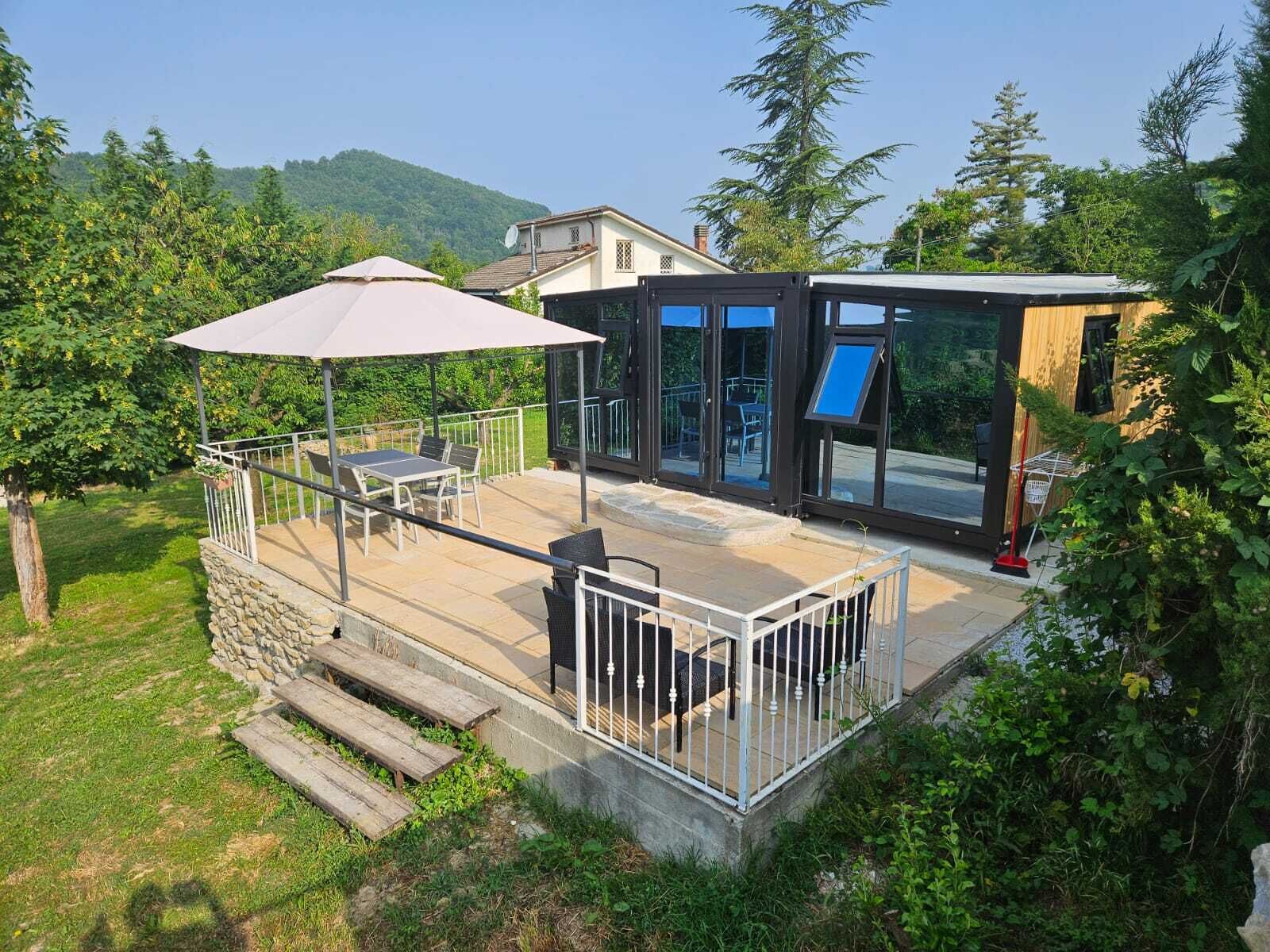 Eine moderne Außenpatio mit Tisch und Stühlen, einer überdachten Sitzgelegenheit und einer gläsernen Struktur.