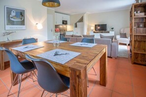 A modern living room with a wooden dining table, blue chairs, a sofa, and a TV.