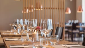 Un comedor con una larga mesa de madera dispuesta para una comida, con copas de cristal transparentes y un centro de mesa con una vela encendida.