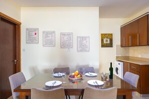 Ein Essbereich mit einem Glastisch, vier Stühlen und einer Obstschale. Drei eingerahmte Speisekarten hängen an der Wand.