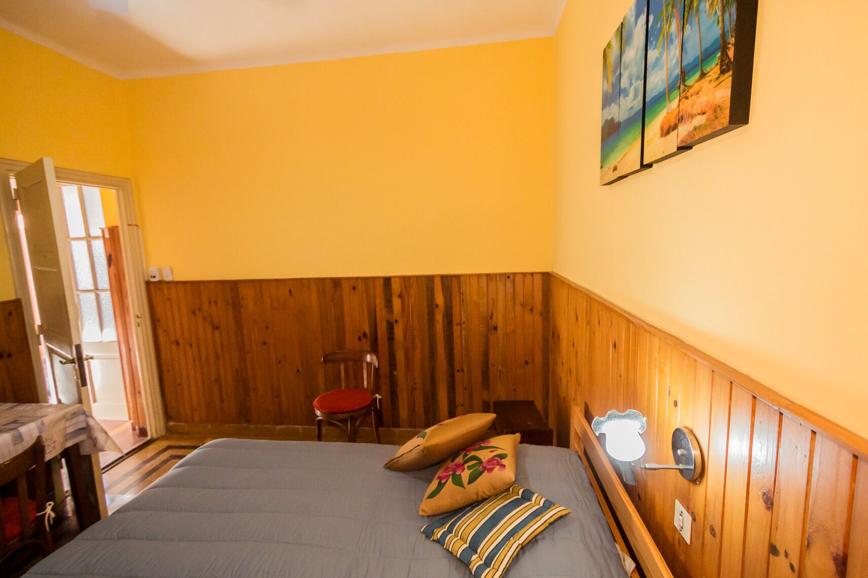 A room with a bed, wooden paneling, a chair, and a painting on the wall.