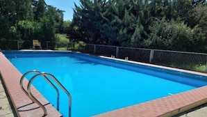 Una piscina rectangular con una escalera metálica en un lado, rodeada por un borde de ladrillo y una cerca de metal.