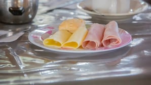Un plato con crepas enrolladas y jamón sobre una mesa con un hervidor y una taza.