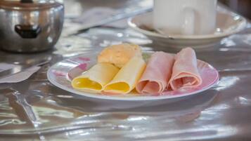 Un plato con crepas enrolladas y jamón sobre una mesa con un hervidor y una taza.