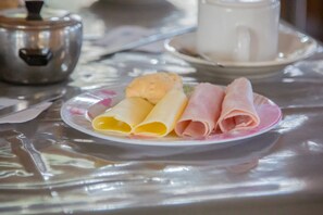 Een bord met gerolde pannenkoeken en ham op een tafel met een theepot en kopje.