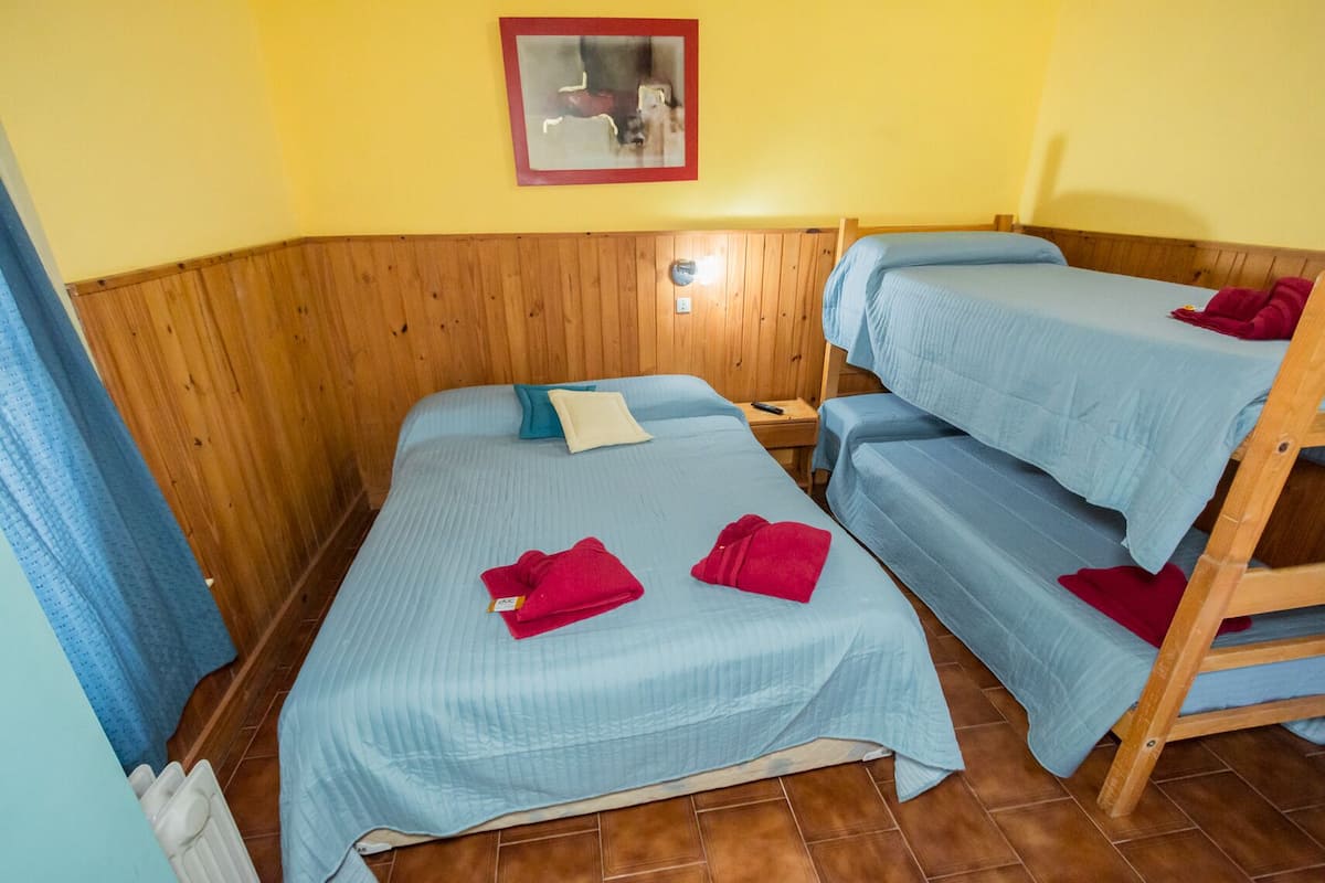 Une chambre avec trois lits, des murs en bois et un mur jaune orné d’un tableau encadré.