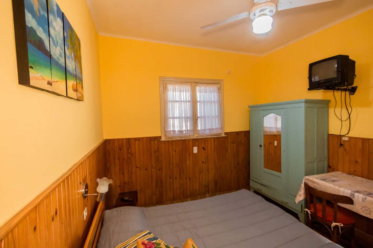 Une pièce comprenant un lit, une fenêtre avec des rideaux, un téléviseur fixé au mur et un meuble.