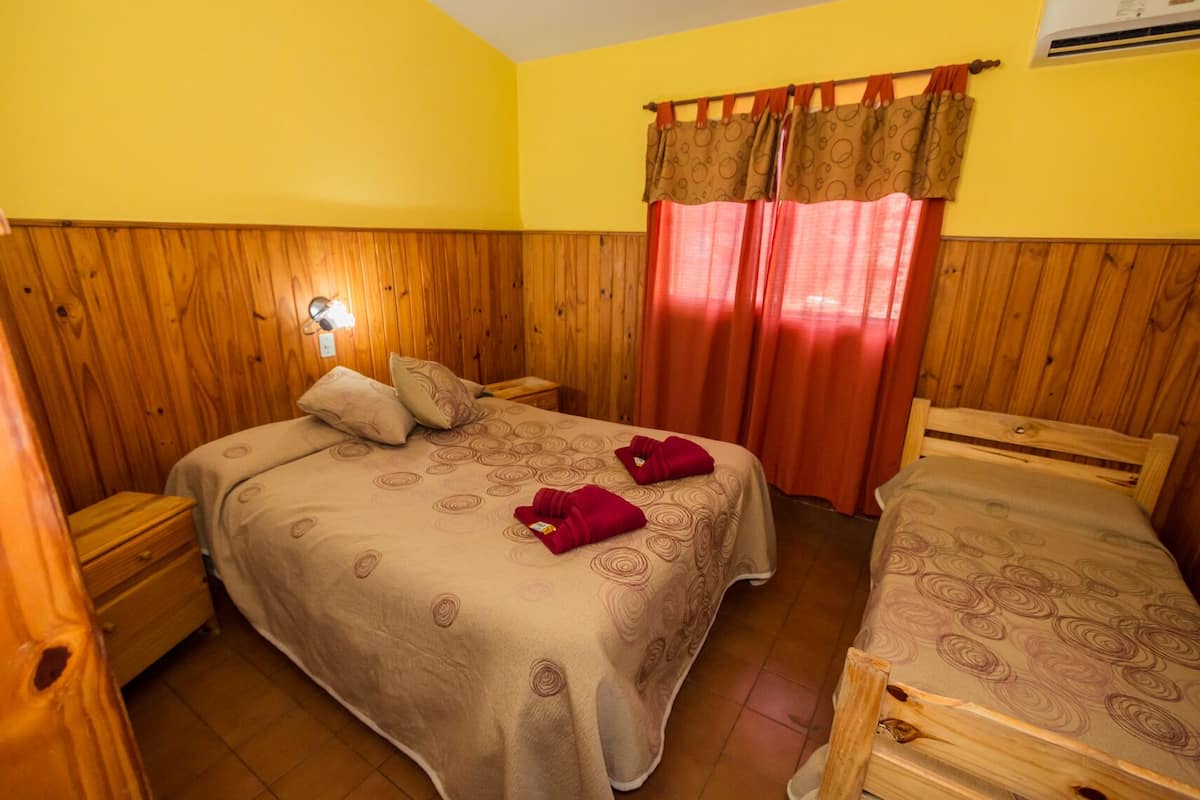 Une chambre avec deux lits, des murs en bois, une fenêtre avec des rideaux et un climatiseur fixé au mur.