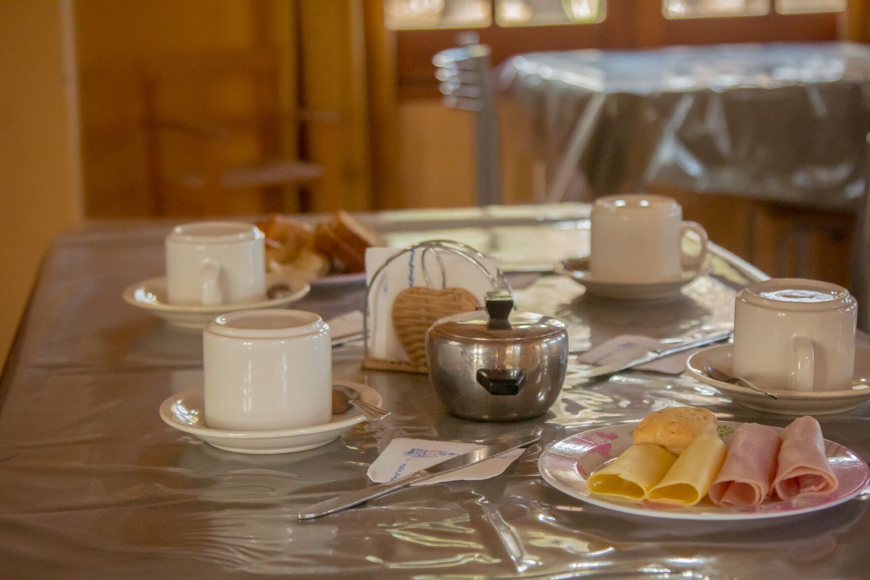 A breakfast setup with cups, a teapot, and pastries on a table.