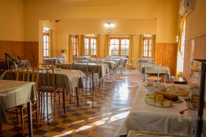 Un espace repas comprenant plusieurs tables et chaises, un sol à carreaux et de grandes fenêtres avec des rideaux.