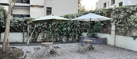 Pátio com piso pavimentado, área de estar externa com mesa e cadeiras e um grande guarda-sol.