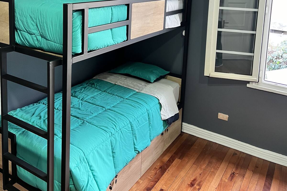 A bunk bed with teal bedding in a room with dark walls and a wooden floor.