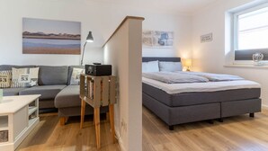 A modern bedroom with a grey bed, a grey sofa, and a small desk with a lamp. - Ferienwohnung in St. Peter-Ording (St. Peter-Ording)