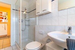 Bathroom features a glass-enclosed shower, toilet, sink, and radiator.