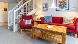 A living room with a staircase, a red sofa, a wooden coffee table, and a painting on the wall.