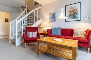 A living room with a staircase, a red sofa, a wooden coffee table, and a painting on the wall.