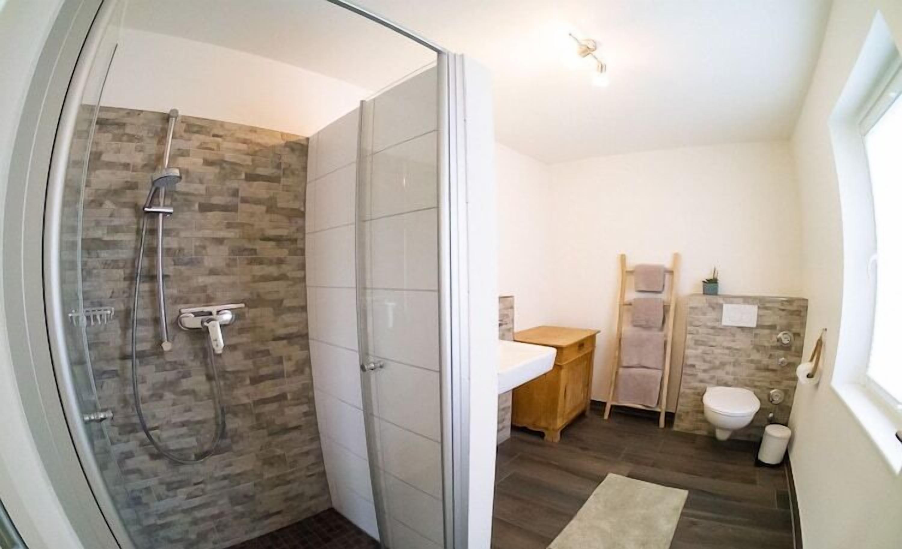Ein modernes Badezimmer mit einer gläsernen Dusche, einem Holzkosmetikschrank, einer Toilette und einem kleinen Waschbecken.