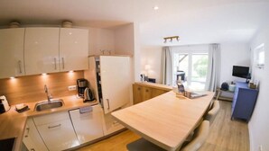 A modern kitchen with white cabinets, a wooden countertop, and a built-in refrigerator. - Ferienwohnung in St. Peter-Ording (St. Peter-Ording)