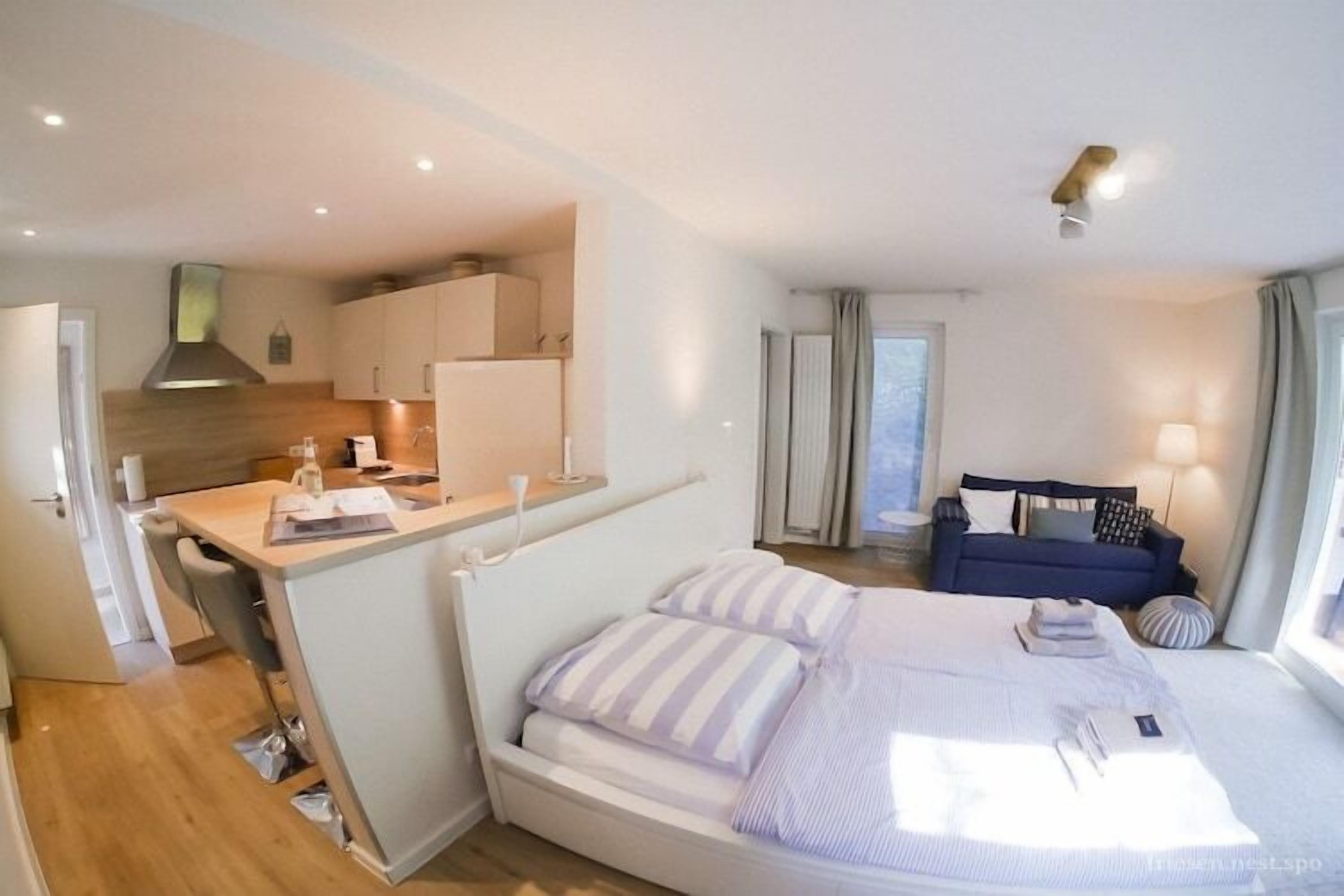 Une chambre d’hôtel de taille réduite, comprenant un lit, une petite kitchenette, un canapé et une fenêtre.