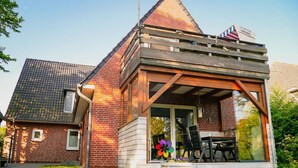 A modern house with a brick exterior, a sloped roof, and a wooden deck with outdoor seating. - Ferienwohnung in St. Peter-Ording (St. Peter-Ording)
