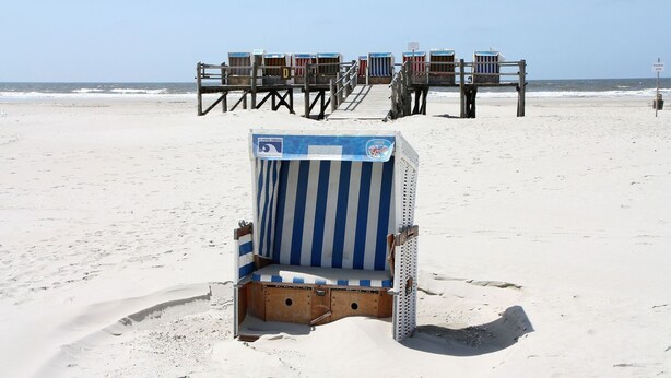 A beach with a striped beach chair and a lifeguard tower in the background. - Ferienwohnung in St. Peter-Ording (St. Peter-Ording)
