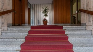 A grand staircase with red carpet and wooden railings, leading to an entrance with a potted plant. - Casa Antonelli by Wonderful Italy (Turin)