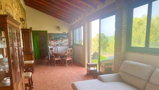 Un salón acogedor con un sofá blanco, una mesa de comedor de madera y sillas, una puerta verde y un cuadro con casas en la pared.