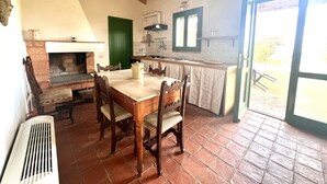 Una cocina rústica con una mesa de madera, sillas, una chimenea y un ventanal grande.