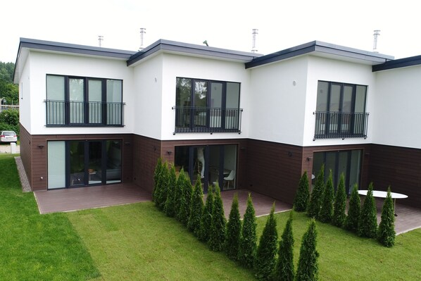 A modern three-story residential building with large windows and balconies, surrounded by a well-maintained lawn and neatly trimmed hedges. - Ferienhaus in Damp am Ostseestrand (Damp)