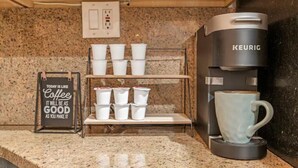 A kitchen with a Keurig coffee maker, a coffee mug, and a shelf with disposable cups.