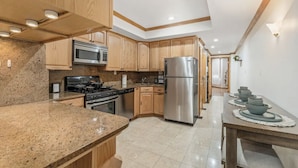 A modern kitchen with granite countertops, stainless steel appliances, wooden cabinets, and a dining area with a table and bowls.