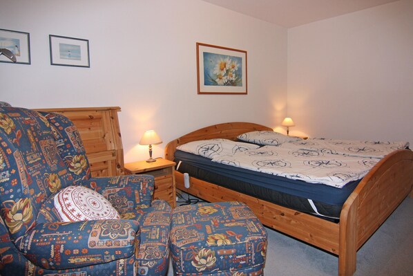 A bedroom with a wooden bed, a patterned sofa, and a nightstand with a lamp.