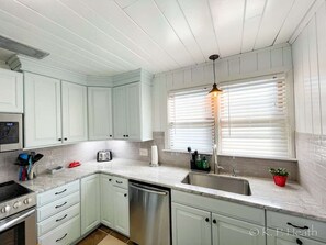 A kitchen with white cabinets, a stainless steel dishwasher, a built-in oven, a sink, and a window with blinds.