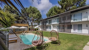 Un edificio moderno con piscina, mobiliario exterior y un césped bien cuidado.