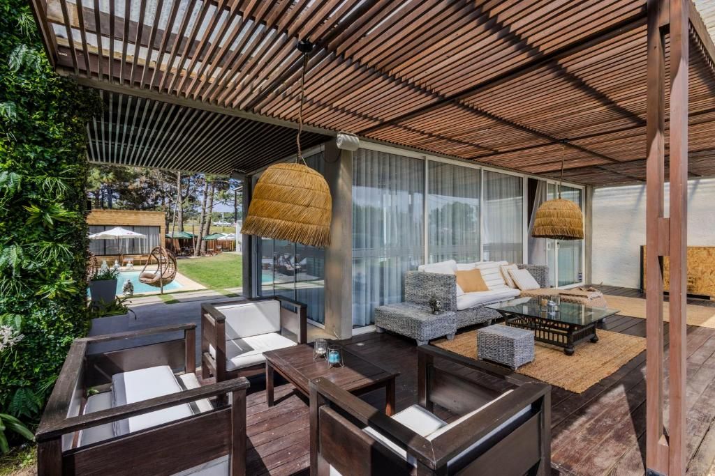 Uma área externa com assentos de madeira, uma mesa de vidro e um lustre de vime suspenso.
