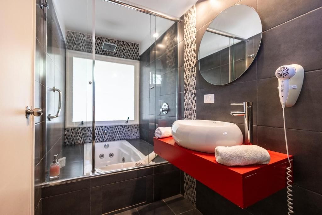 A modern bathroom with a glass-enclosed shower, a large mirror, and a red vanity with a towel.