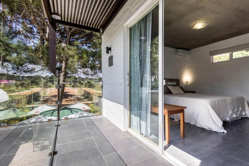 A modern bedroom with a large sliding glass door leading to a balcony, a bed with a white bedspread, and a small wooden table.