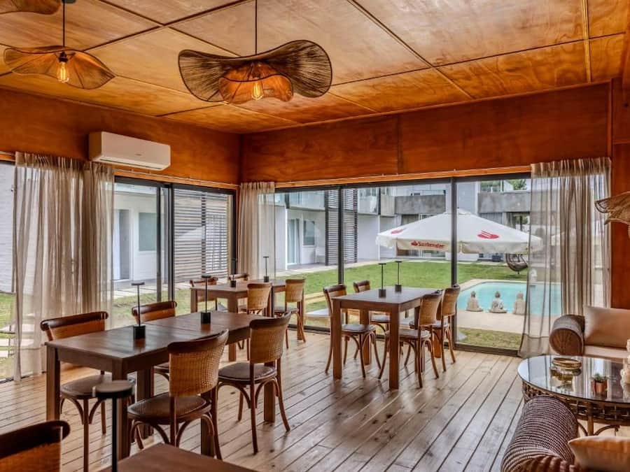 A spacious indoor area with wooden flooring, tables, and chairs arranged for dining. Large windows provide views of the outside.