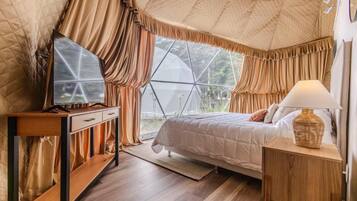 Ein Schlafzimmer mit Bett, Schreibtisch, Lampe und einem fenster mit Vorhängen.