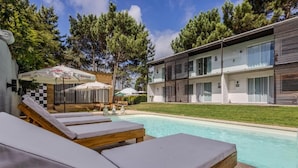 Zona junto a la piscina con sillones de descanso, una piscina y un edificio con varios balcones.