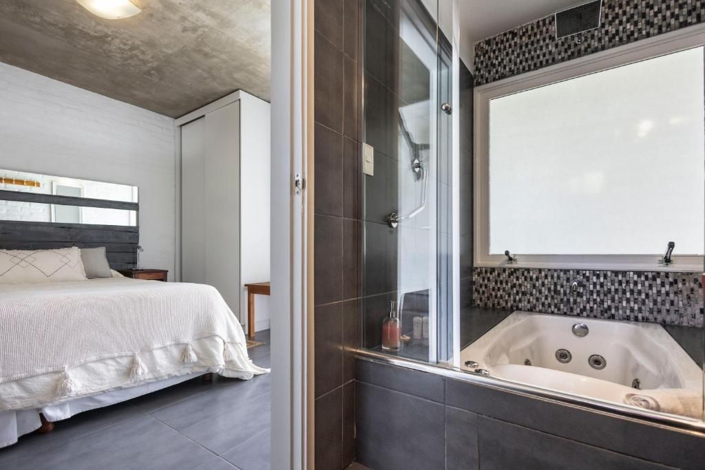 A modern bathroom with a large bathtub, a shower enclosure, and a bed with a white headboard.