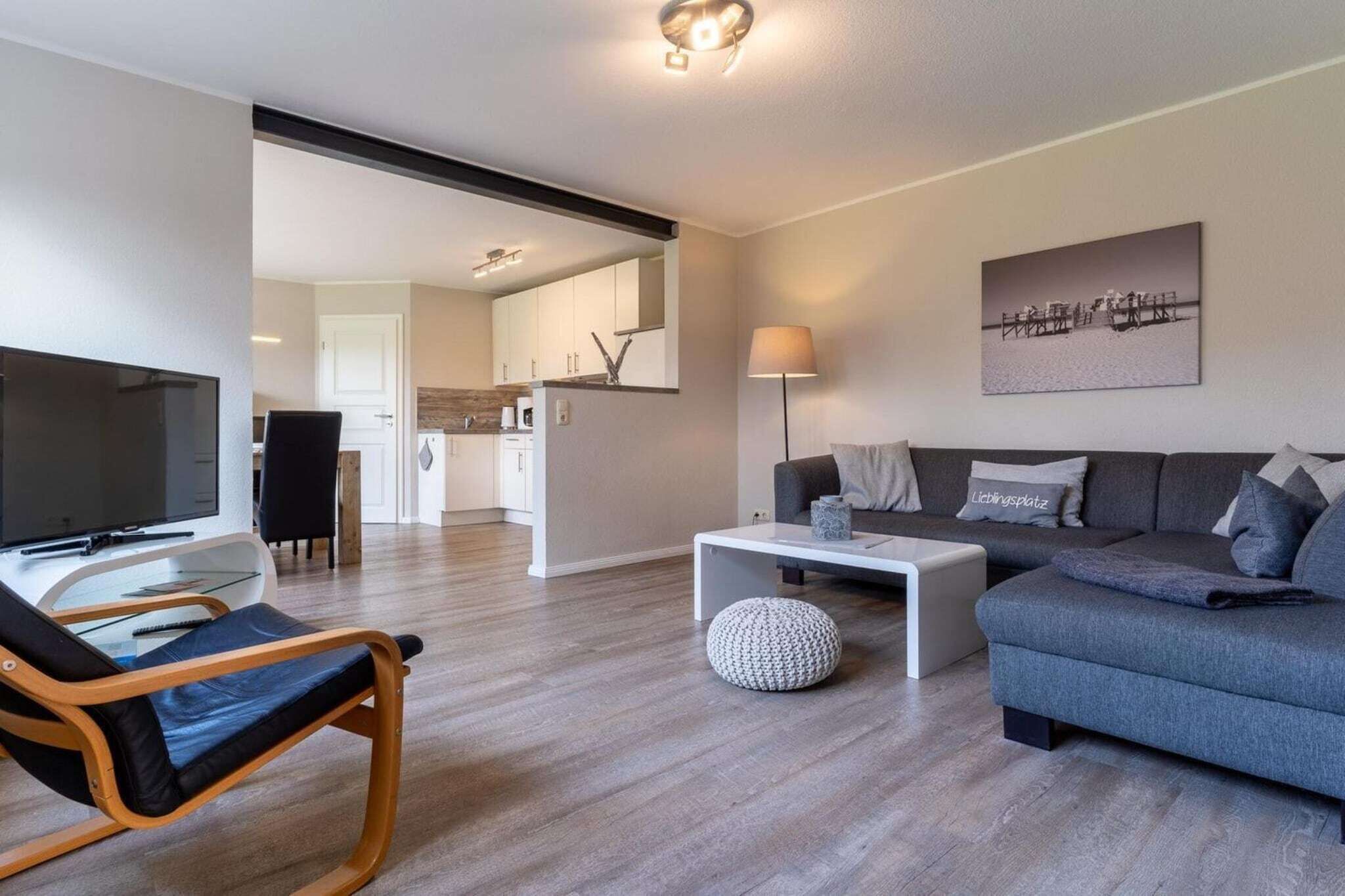 Ein modernes Wohnzimmer mit einem Flachbildfernseher, einem Sofa, einem Couchtisch und einem Essbereich im Hintergrund.