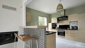 A modern kitchen with a central island, stainless steel appliances, and a hanging light fixture. - Holiday Home in Terenez with Sea Views (Plougasnou)